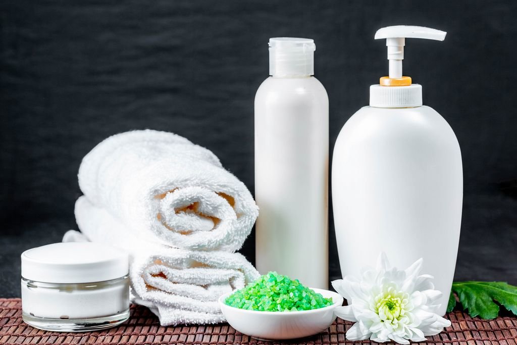 Spa-Utensilien für Hautpflege wie Creme, Seife und Badesalz mit Badetuch vor dunklem Hintergrund