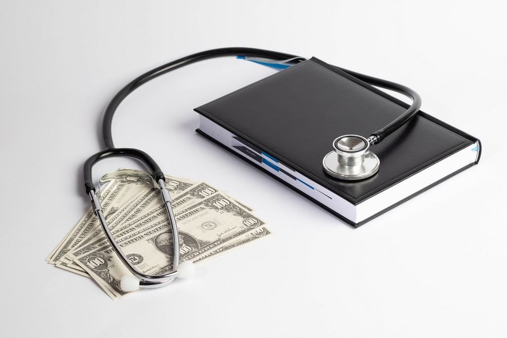 Stethoskop auf schwarzem Buch und Banknoten = Gesundheitskosten / medizinische Kosten