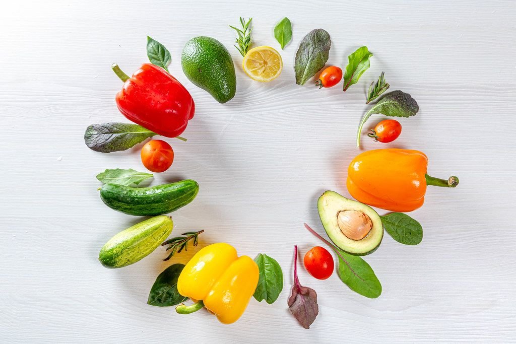 Buntes Frischgemüse liegt in einem Kreis auf einem weißen Holzhintergrund
