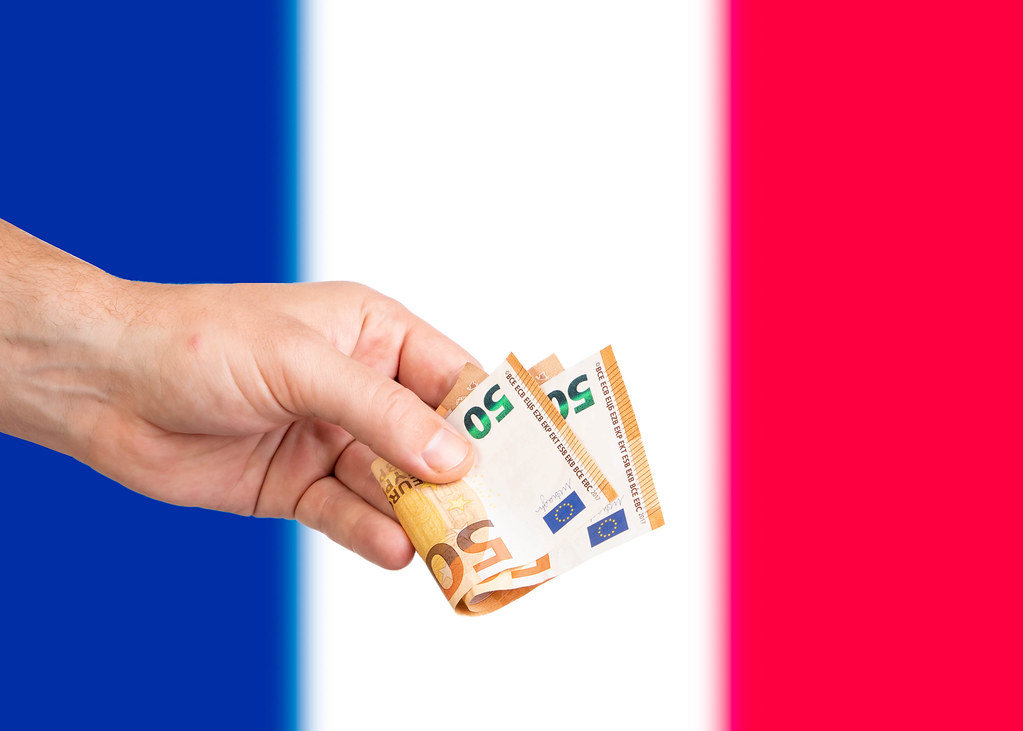Hand with Euro banknotes over flag of France