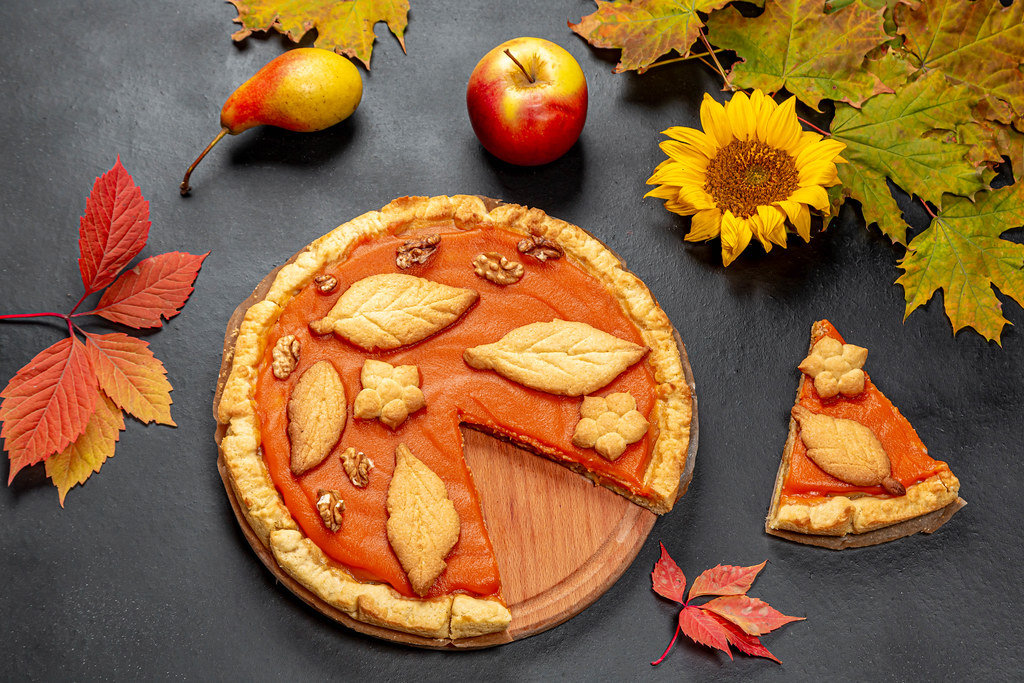 Beautiful decorated pumpkin pie on black background with autumn leaves, apple and sunflower flower