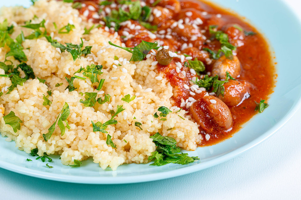 Closeup cereal couscous with spacely in tomato sauce and sesame seeds