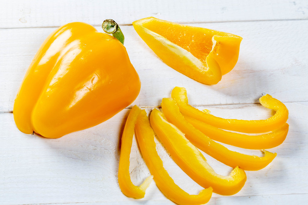 Fresh orange bell pepper on a white wooden background