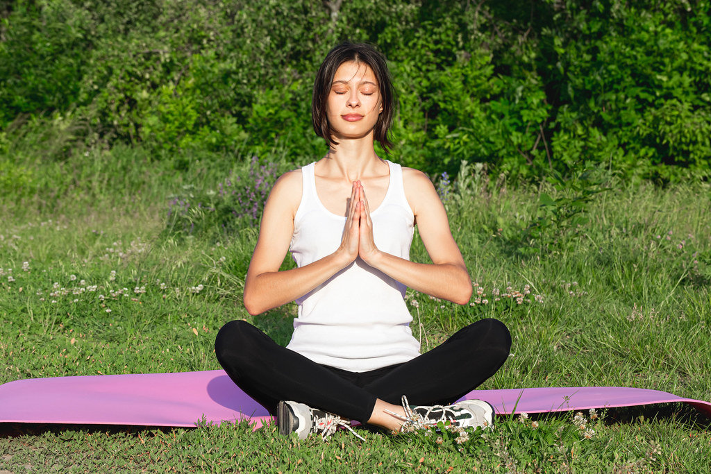 A woman in the Siddhasana position is engaged in meditation in nature