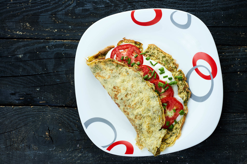 Freshly cooked omelet with herbs, sour cream and tomatoes