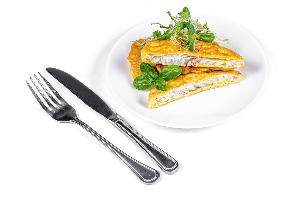 Slices fried fish in batter with fresh micro greens on a white background with a knife and fork