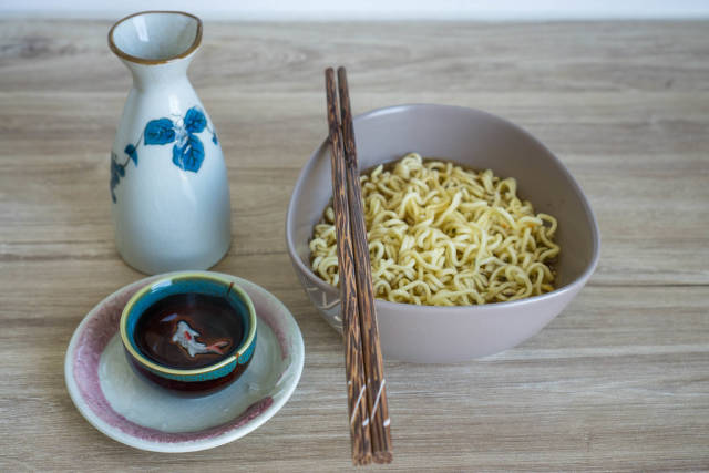 Instant Noodle Soup in a Bowl with Chopsticks and small Tea Cup on a Wodden Table