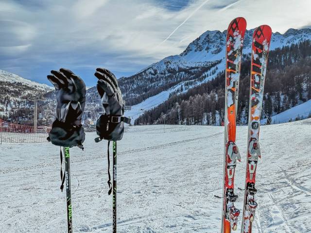 Skiausrüstung wie Paar Ski, Skistöcke und darauf gesteckte Handschuhe auf Skipiste im Winter