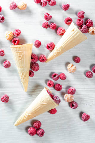 Top view of waffle cone with frozen raspberry berries on white wooden background