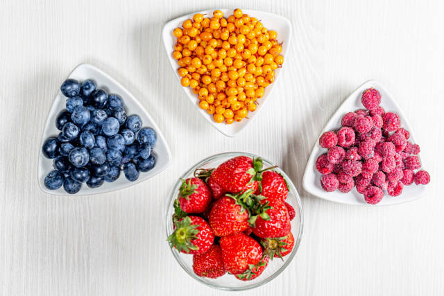 Ripe sea buckthorn berries, blueberries, raspberries and strawberries on a white wooden background. Top view