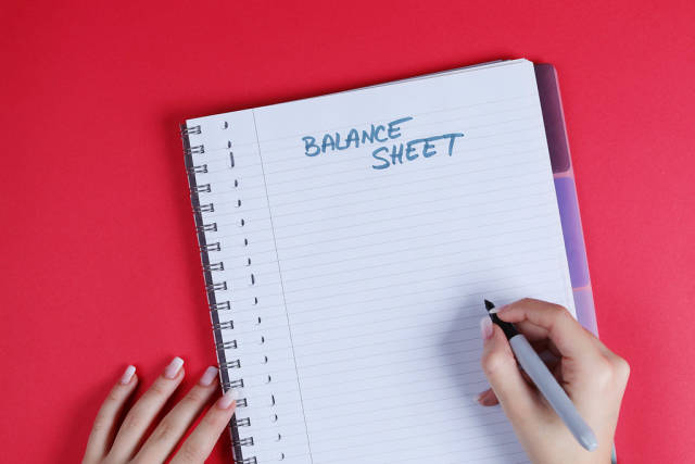 Woman writing Balance Sheet text on notebook, red background