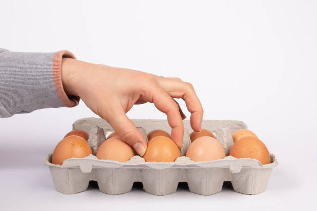 Woman hand selected egg in egg carton on white background