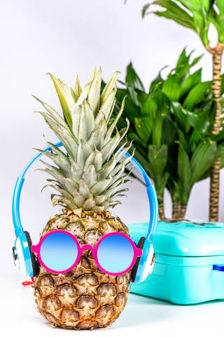 Pineapple in sunglasses and headphones with a suitcase and palm trees in the background