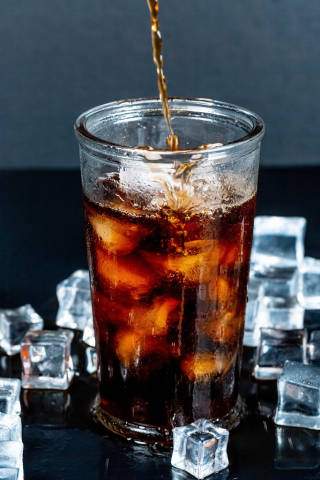 Brown carbonated drink is poured into a glass with ice