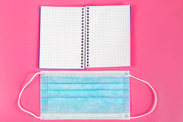 Open notepad and medical mask on pink background, top view