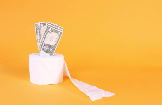 Toilet paper with dollar banknotes on orange background
