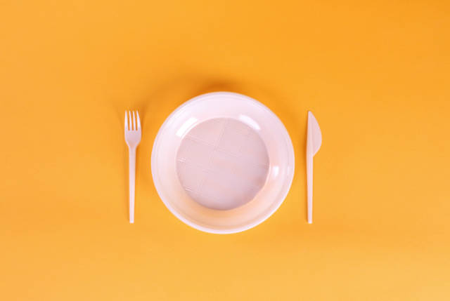 White plastic plate, fork and knife on orange background