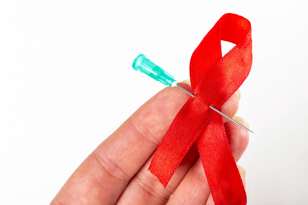 Red ribbon with needle in woman hand. World Aids Day concept
