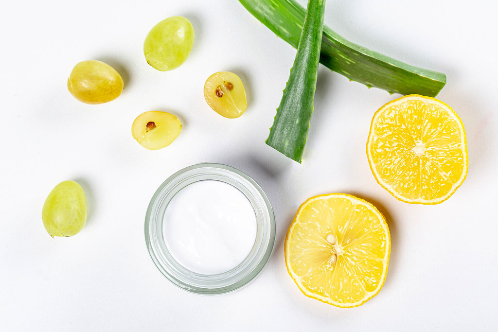 Top view, a jar of cream on a white background with fresh grapes, lemon slices and aloe