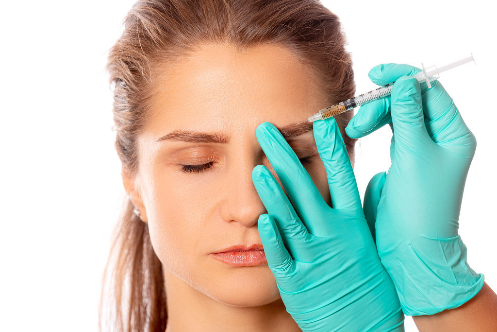 Doctors hands in gloves make an injection into the eyebrow of a girl
