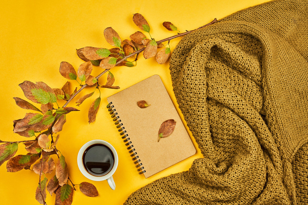 Cozy fall atmosphere with a cup of coffee, autumn leaves and warm sweater