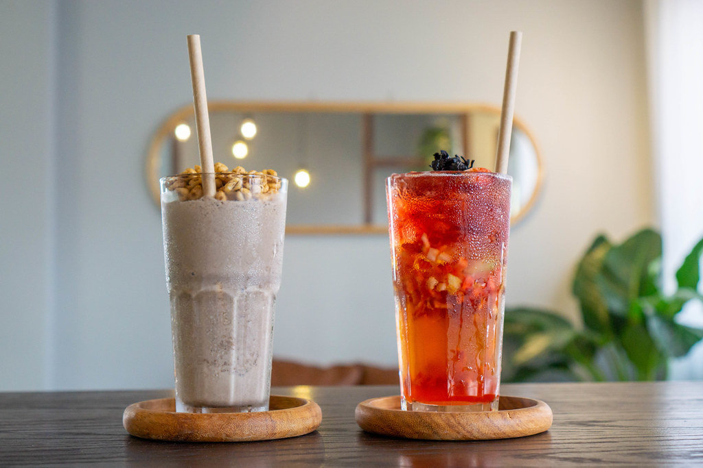 Close Up Photo of Cookies and Cream Milkshake and Strawberry Iced Tea in Cocktail Glasses on Wooden Saucers with Paper Straws in a Cafe