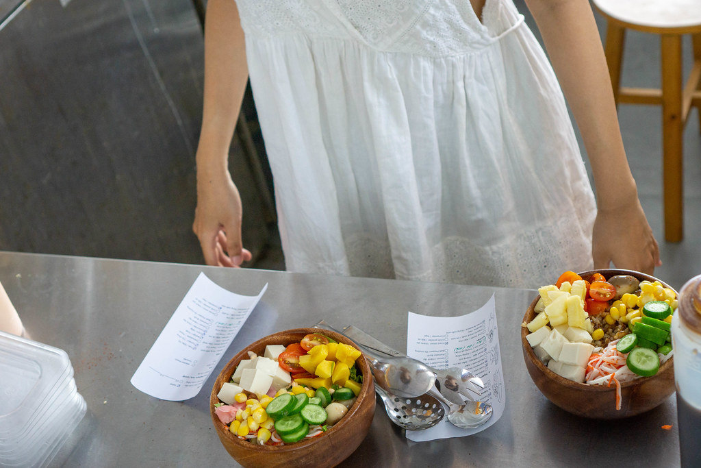 Kitchen Staff preparing Healthy Hawaiian Poke Bowls with Fresh Vegetables and Fruits with Ingredients Lists from Customers