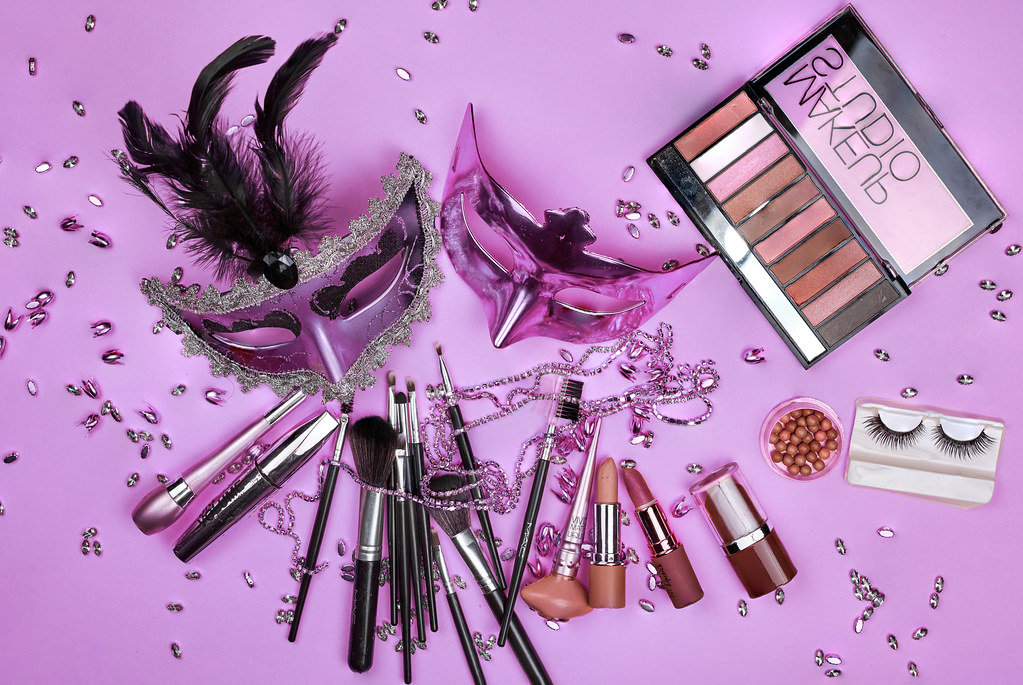Mardi Gras carnival masks and female make-up tools set on purple background