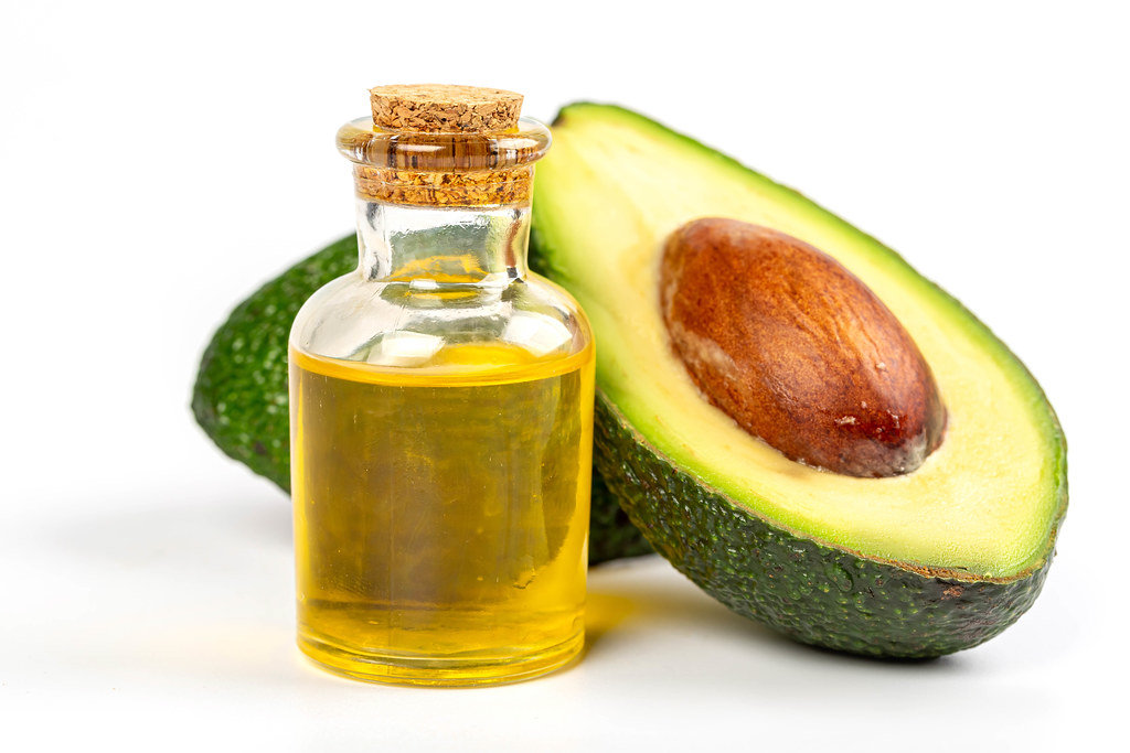 Bottle of avocado essential oil with fresh half avocado, close up