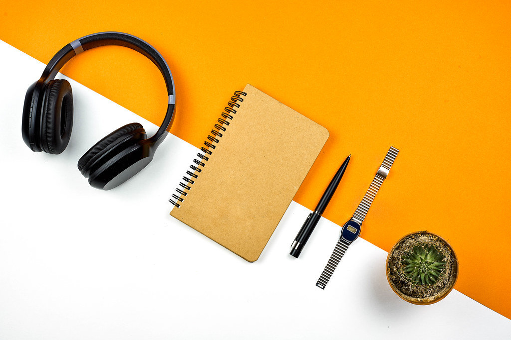 Bright workspace. Wireless headphone, notepad, wristwatch and cactus from above
