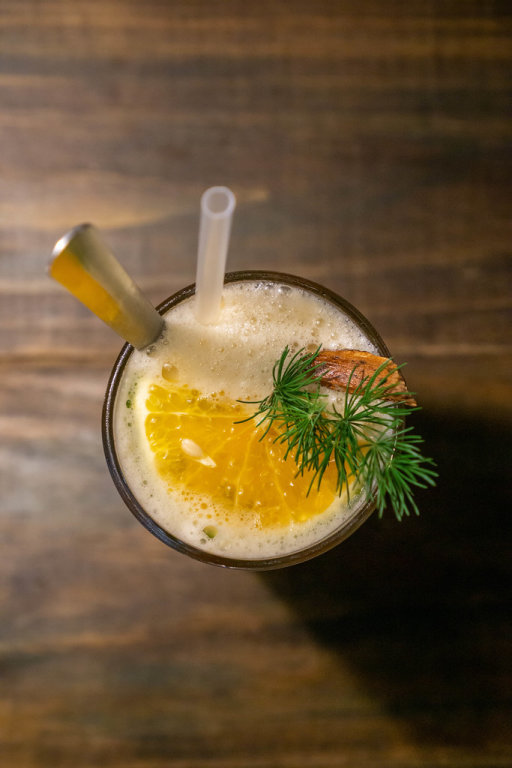 Top View Photo of Iced Orange-Cinnamon Tea with Slice of Orange, Rosemary, Spoon and Straw in a Cocktail Glass