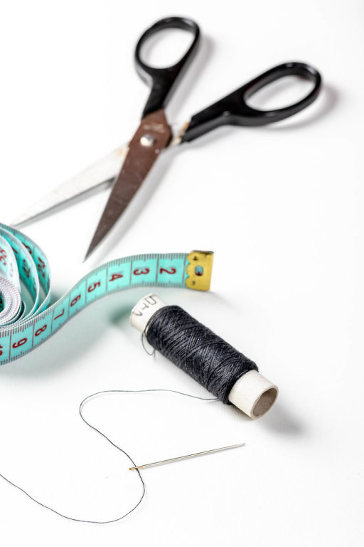 Scissors, measuring tape and a spool of black thread with a needle