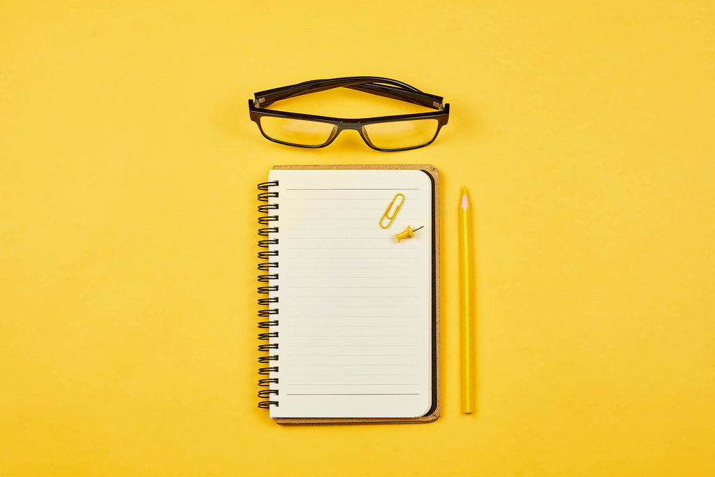 Starting a diary. Open notepad with eyeglasses on yellow background