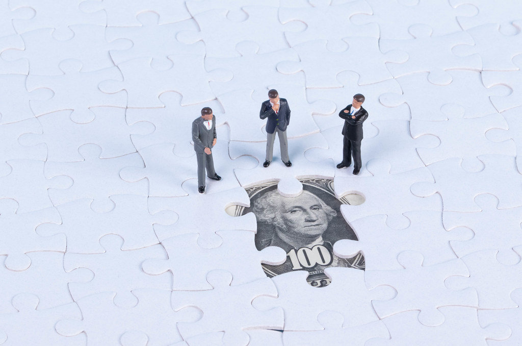 Group of businessman with missing jigsaw puzzle pieces on money dollar background