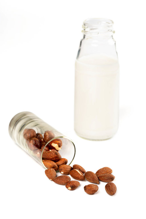 Almond milk in glass bottle with almond nuts on white. Vegetarian eating