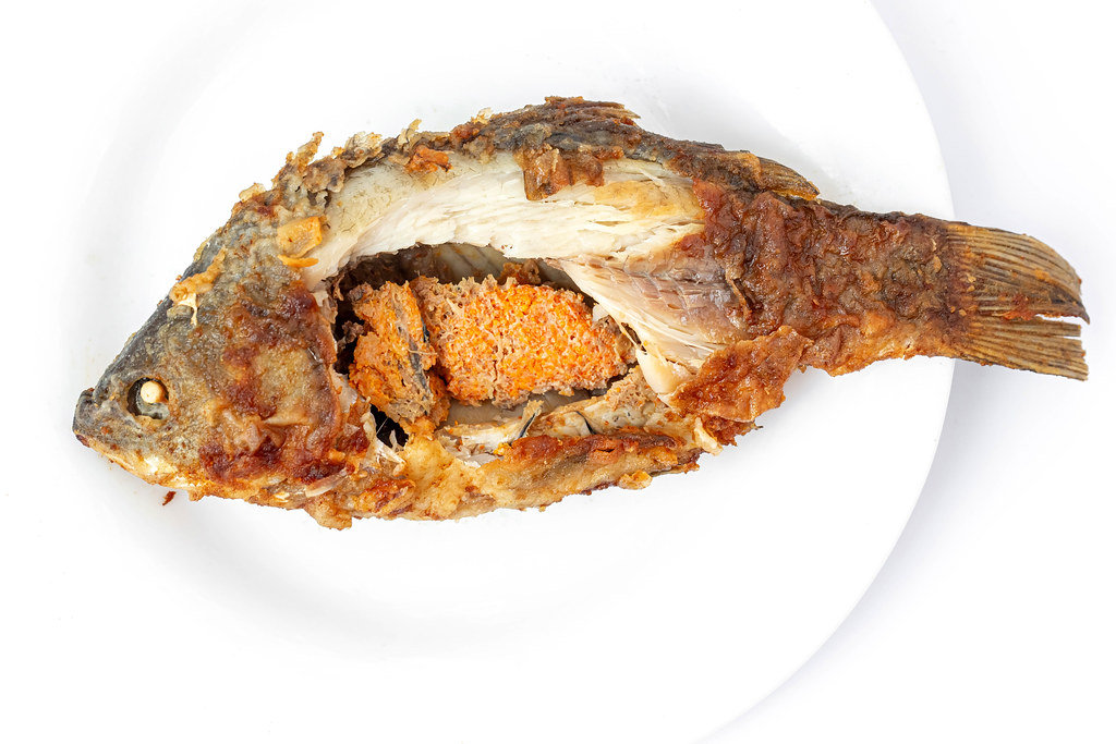 Top view of fried crucian carp with caviar on a white plate