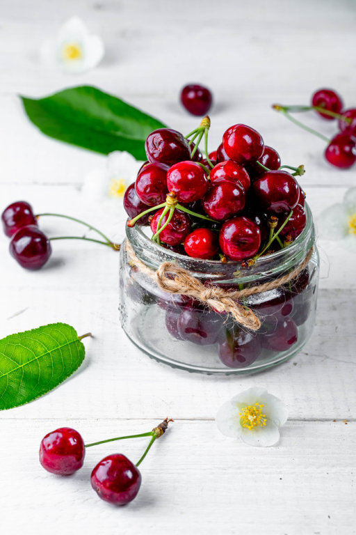 Glass jar with cherries on white wooden background