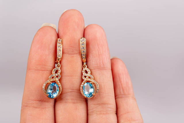 Pair of gold earrings with blue topaz in a female hand
