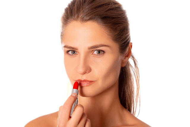 Makeup concept, woman holds red lipstick in hand near lips