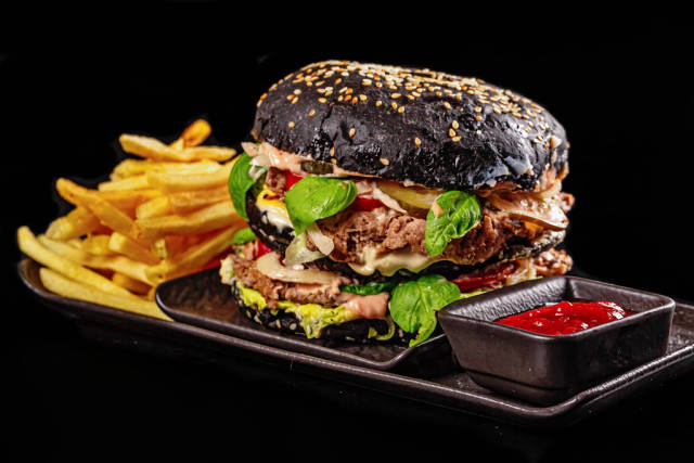 Fresh hamburger with black bun, cutlets, sauce and vegetables served with fries and ketchup