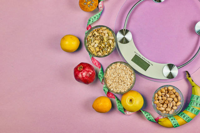 Healthy nutrition. Scales, fruits and nuts on pink background