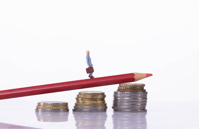 Man walking on a red pencil laying on a stack of coins