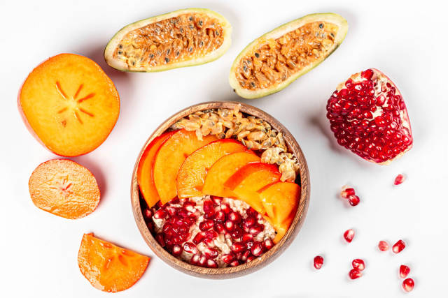 Top view, bowl of oatmeal on white background with pomegranate, persimmon and kuruba