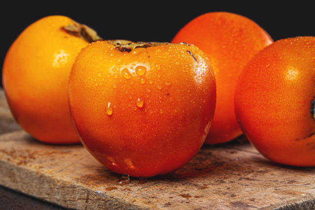 Orange ripe persimmon fruits with water drops on dark background