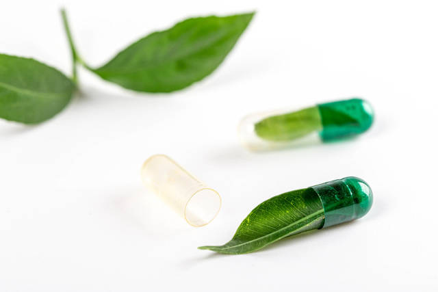 Close-up, open medical capsule with a fresh green leaf inside