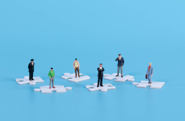 Miniature people standing on white jigsaw puzzle pieces