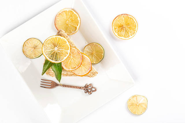 Honey cake with condensed milk on a white plate with a fork and dried lemon and lime, top view