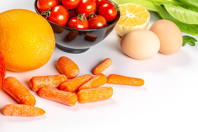 Orange, cherry tomatoes, carrots, pak choy cabbage, lemon and eggs on white