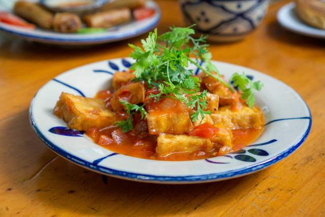 Close Up Food Photo of Vietnamese Dish with Tofu, Tomato Sauce, Parsley and Spices on a Ceramic Plate in a Restaurant
