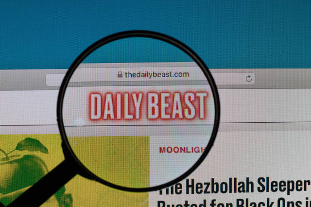 Daily Beast Logo und offizielle URL der Internetseite, vergrößert dargestellt unter einer Lupe